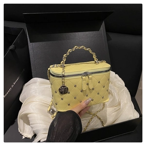 Detailed view of yellow quilted handbag with metal rivets and rose charm in a gift box