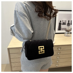 Detail of black quilted shoulder bag with gold geometric clasp worn over the shoulder