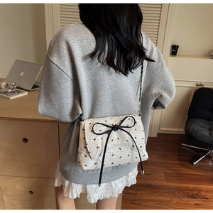 Detail of white quilted crossbody bag with black bows and silver chain on female model