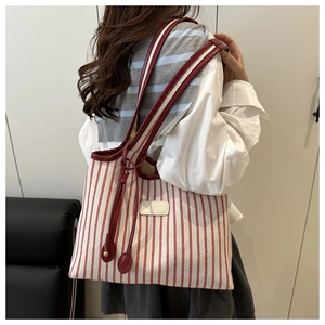 Close-up of red and white striped canvas tote bag with leather straps and gold metal details