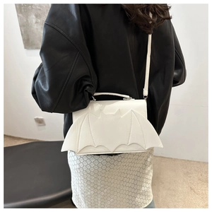 Close-up of white bat wing crossbody bag styled on black leather jacket outfit