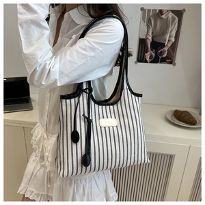 Detail of striped canvas tote bag with black leather straps in a cozy office setting