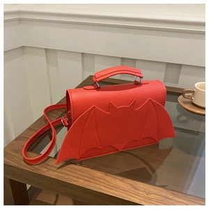 Detail of red bat-shaped crossbody bag with wing stitching on a wooden table