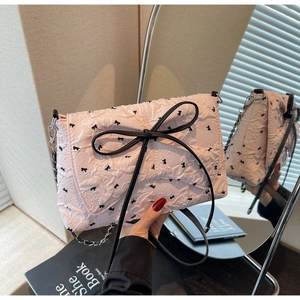Detail of pink quilted crossbody bag with black ribbon bow and metal chain strap