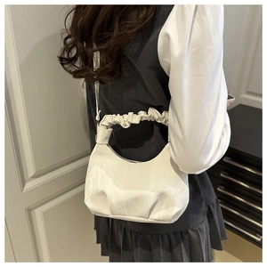 Detail of white pleated cloud handle and textured synthetic leather on a crescent bag