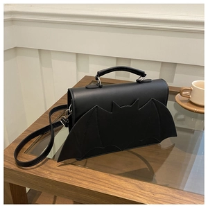 Macro shot of gothic black bat-wing shaped handbag on a glass table with leather strap