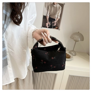 Detail of black corduroy bucket bag with red cherry print and golden zipper closure