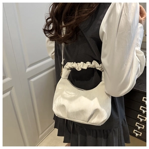 Detail of cream crescent bag featuring a ruched handle and sleek faux leather finish