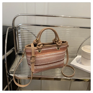 Detail of woven straw bucket bag with brown leather handles and striped texture on a shelf
