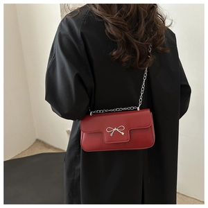 Detail of red square crossbody bag with silver bow buckle and chain strap on black coat