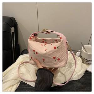 Close-up of pink corduroy bucket bag with embroidered cherries and metal button