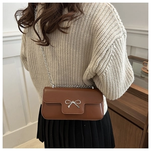 Close-up of brown leather bag with silver bow buckle and chain strap on a model