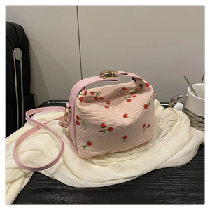 Close-up of pink corduroy bucket bag featuring red cherry patterns and gold metal clasp