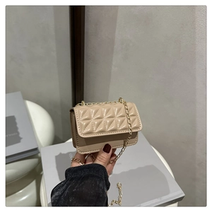 Close-up of beige quilted mini chain bag held by hand, featuring elegant gold hardware