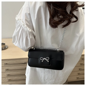 Detail of a black leather crossbody bag featuring a silver bow clasp and chain strap