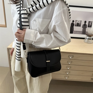 Minimalist black leather crossbody bag with gold hardware shown on a model