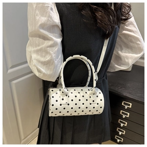 Detailed side view of white polka dot cylinder crossbody bag worn by a model in a room