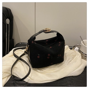 Detail of black corduroy bucket bag featuring red cherry embroidery and gold twist lock
