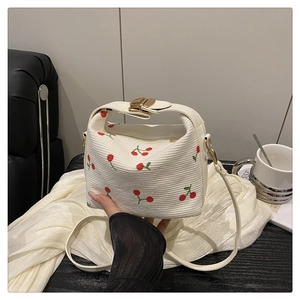 Detailed close-up of cream bucket bag featuring cherry prints and golden metal buckle