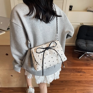 Chic white quilted crossbody bag with black bow and chain strap on a model