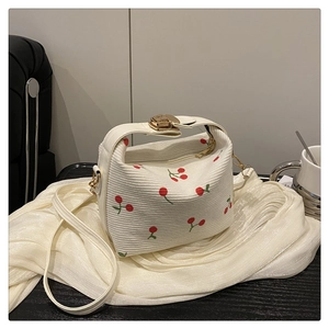 Detail of cream bucket bag with red cherry embroidery and gold metal buckle strap