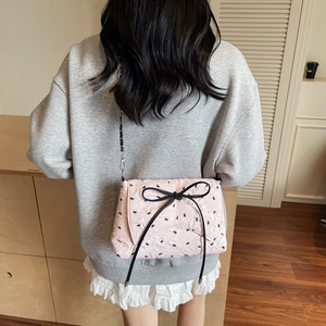 Pink quilted crossbody bag with floral pattern and black tassel bow on chain strap