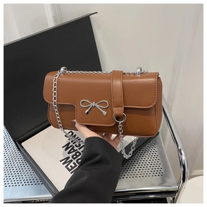 Detail of a brown leather shoulder bag featuring a silver bow buckle and chain strap