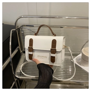 Detail of white and brown contrast square bag with golden buckles and refined stitching