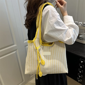 Large yellow and white striped canvas tote bag carried by a model against a white wall