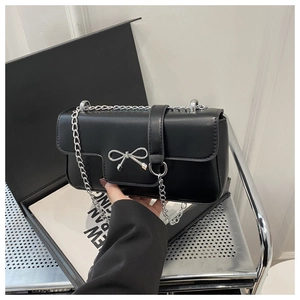 Detail of black crossbody box bag featuring silver metallic bow clasp and delicate chain strap