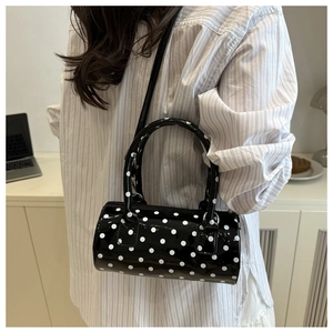 Close-up of black and white polka dot Boston bag worn crossbody with glossy finish