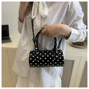 Chic black polka dot cylinder crossbody bag styled on a white outfit in a modern setting