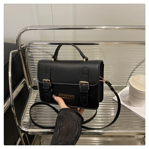 Detailed shot of black minimalist crossbody bag with double buckles on a metal stand