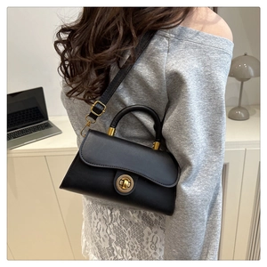 Model view of black leather trapezoid handbag with gold clasp and adjustable strap