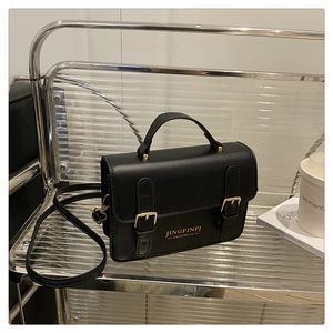 Detail of black crossbody bag with gold buckles and detachable strap on display stand