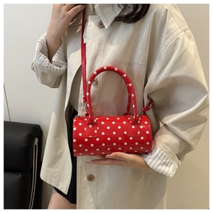 Detail of red and white polka dot cylinder crossbody bag with glossy patent finish