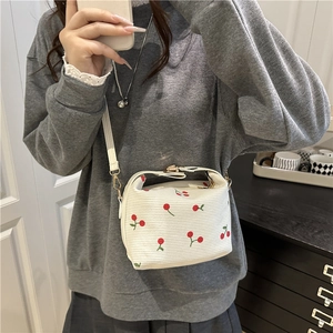 White bucket crossbody bag with red cherry print and textured finish on a shoulder strap