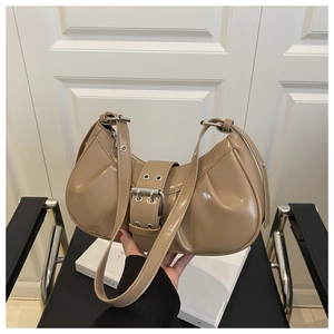 Detail of beige patent leather crescent bag with wide buckled strap and silver eyelets