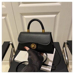 Detail of a black crossbody bag with a vintage gold circular twist lock on a leather surface