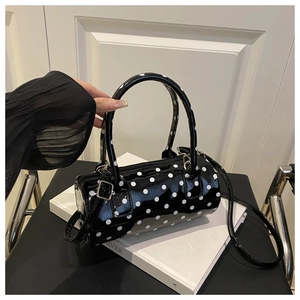 Detail of a black polka dot cylinder bag with silver hardware on a white book