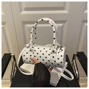 Detailed close-up of a white polka dot barrel bag with glossy patent leather texture