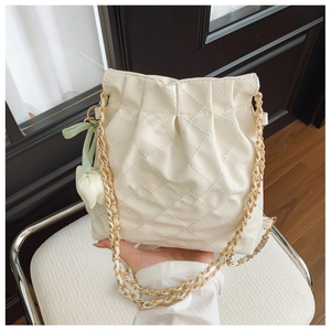 Close-up of beige quilted leather bucket bag with gold chain and tulip floral pendant