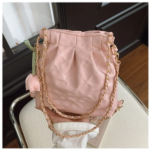 Detail of pink quilted bucket bag with chain strap and tulip charm in model's hand