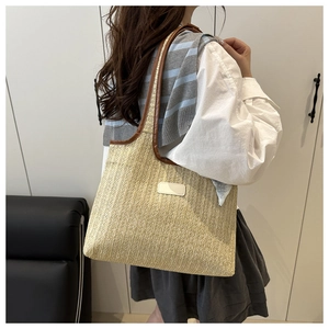 Detail of woven straw tote bag featuring brown leather trim and shoulder straps on a model