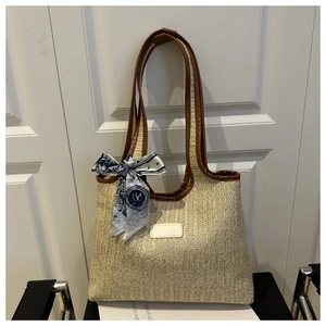 Detail of beige woven tote bag with brown leather handles and a blue patterned silk scarf