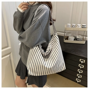Model wearing a large striped canvas tote bag with wide shoulder strap in daily setting