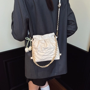 Beige quilted drawstring bucket bag with gold chain and floral charm on model