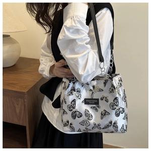 Détail de la broderie papillon et chaîne métallique sur un sac d'épaule en satin