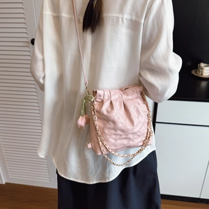 Pink quilted bucket bag with floral charm and chain strap shown on model's shoulder