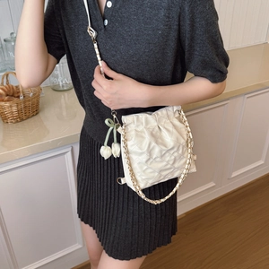 Chic quilted cream bucket bag with gold chain strap and floral charms on a model